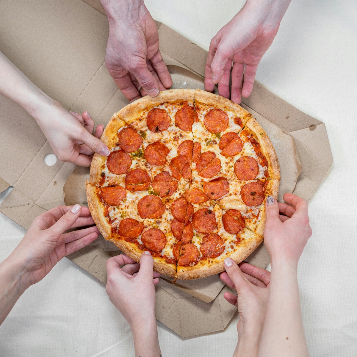 Hands reaching for slices of a pepperoni pizza